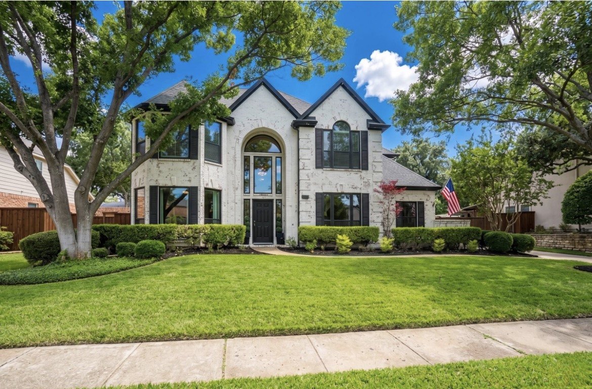 Two-story white brick home with a manicured lawn on a tree-lined street